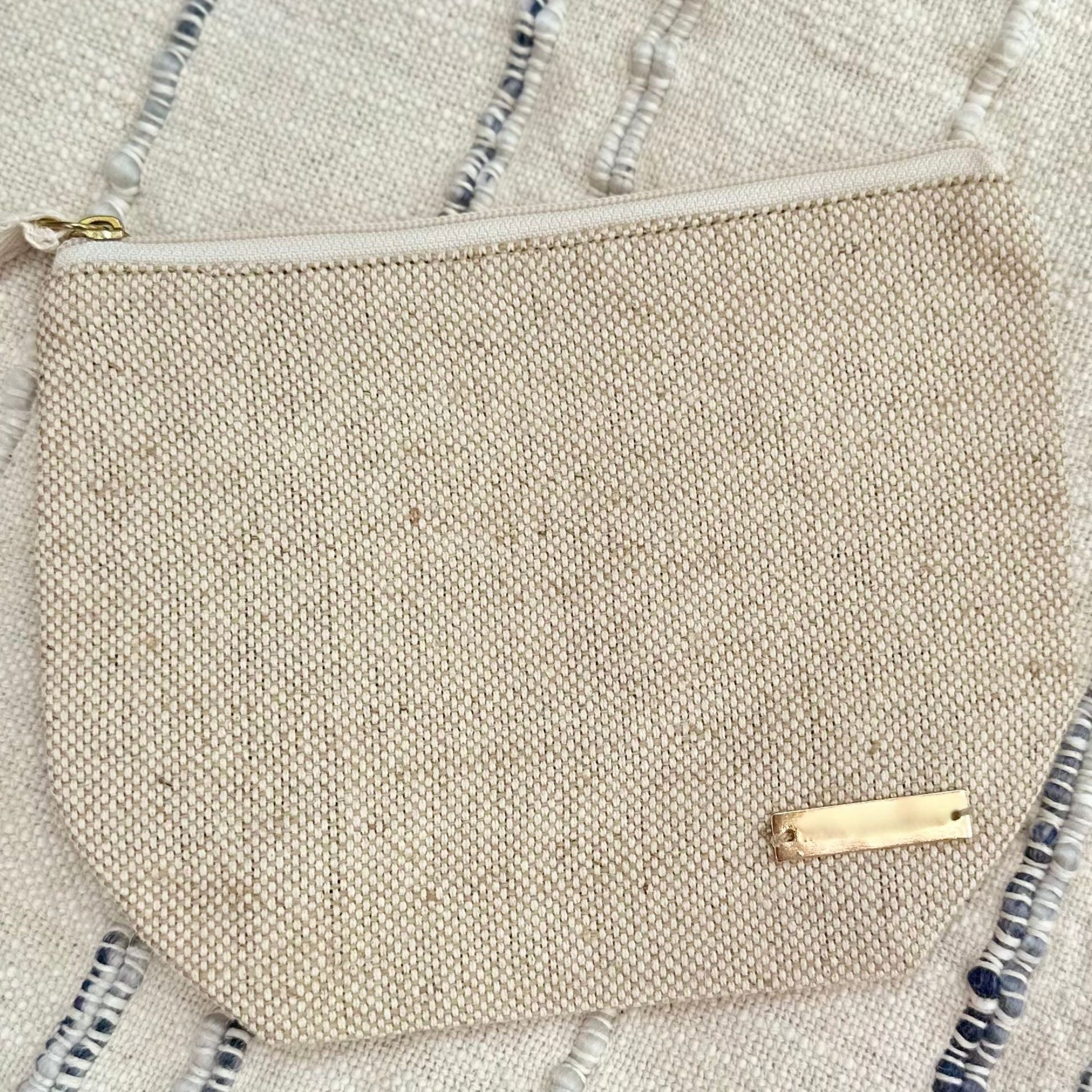 Small beige wet bag with a gold zipper on a neutral background