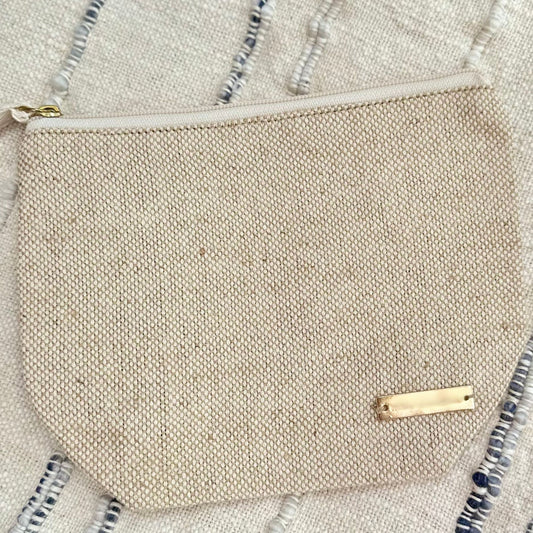 Small beige wet bag with a gold zipper on a neutral background