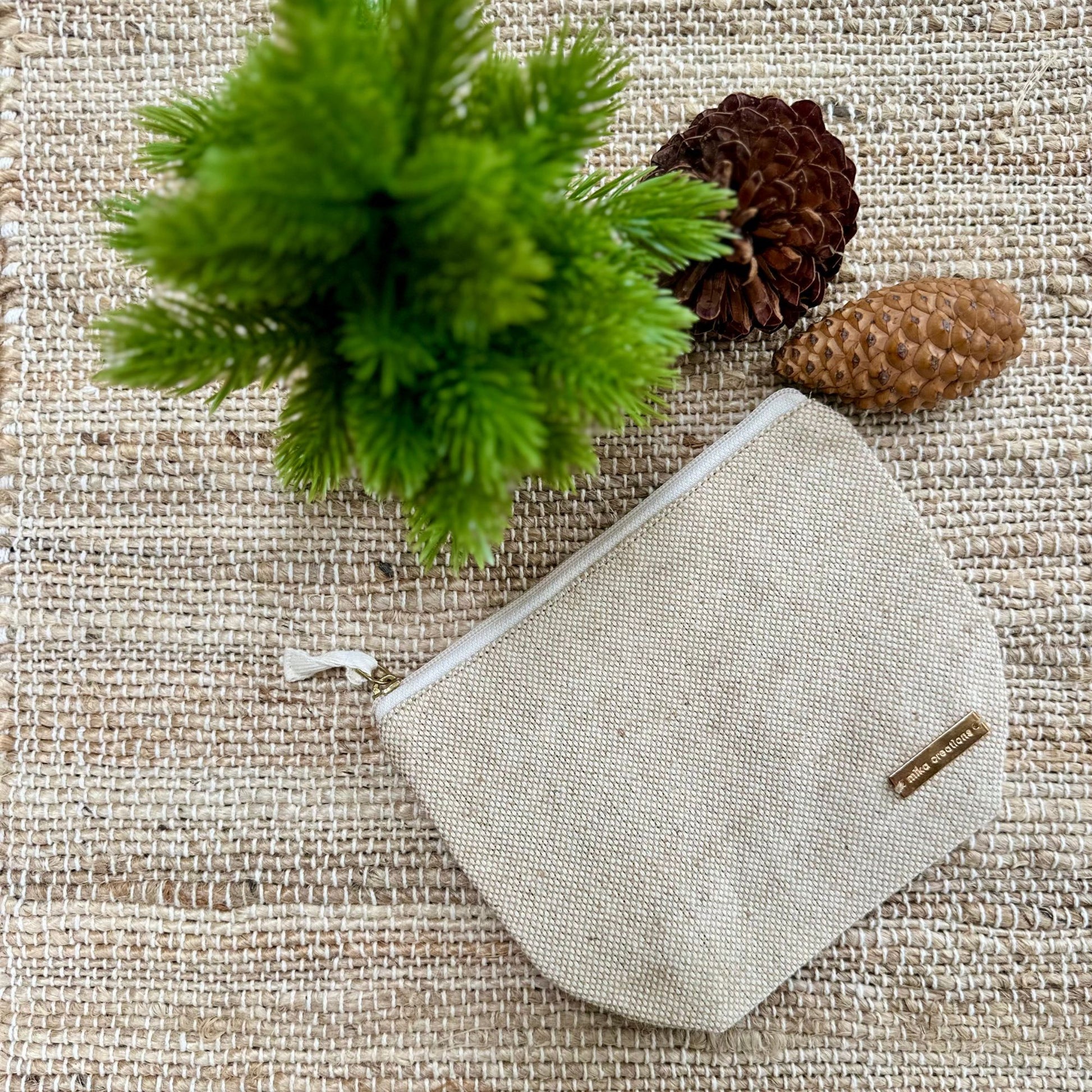 Textured pouch with a brand logo on a textured surface with greenery and pine cones.